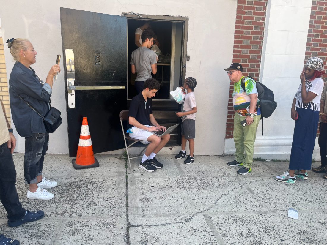 Liam taking sign-ups on a laptop as a child receives a meal outside the Mount Vernon kitchen