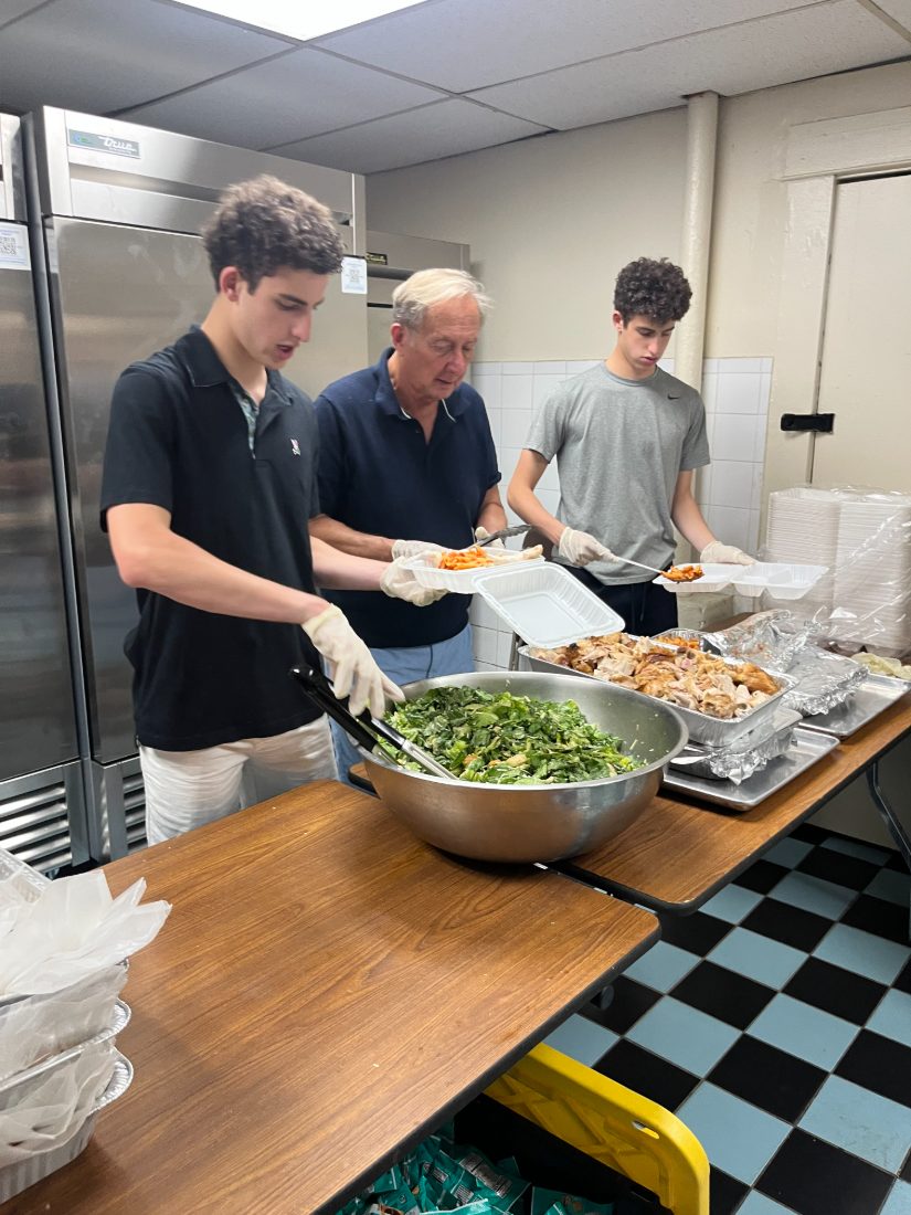 Daniel and Liam serving salad and chicken alongside a volunteer