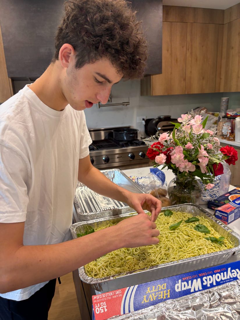 Liam garnishing trays of pesto pasta with fresh basil